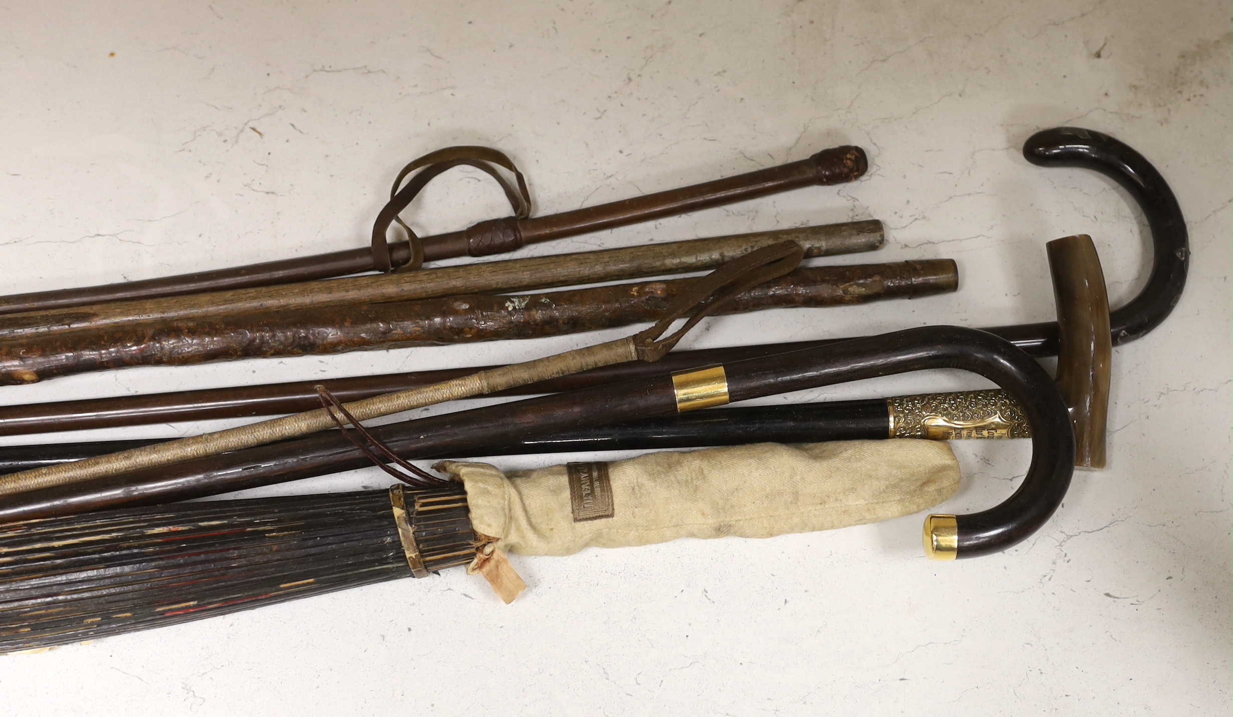 A horn handled presentation metal mounted walking stick, four others, two riding crops and a paper parasol, presentation walking sick 91 cm long